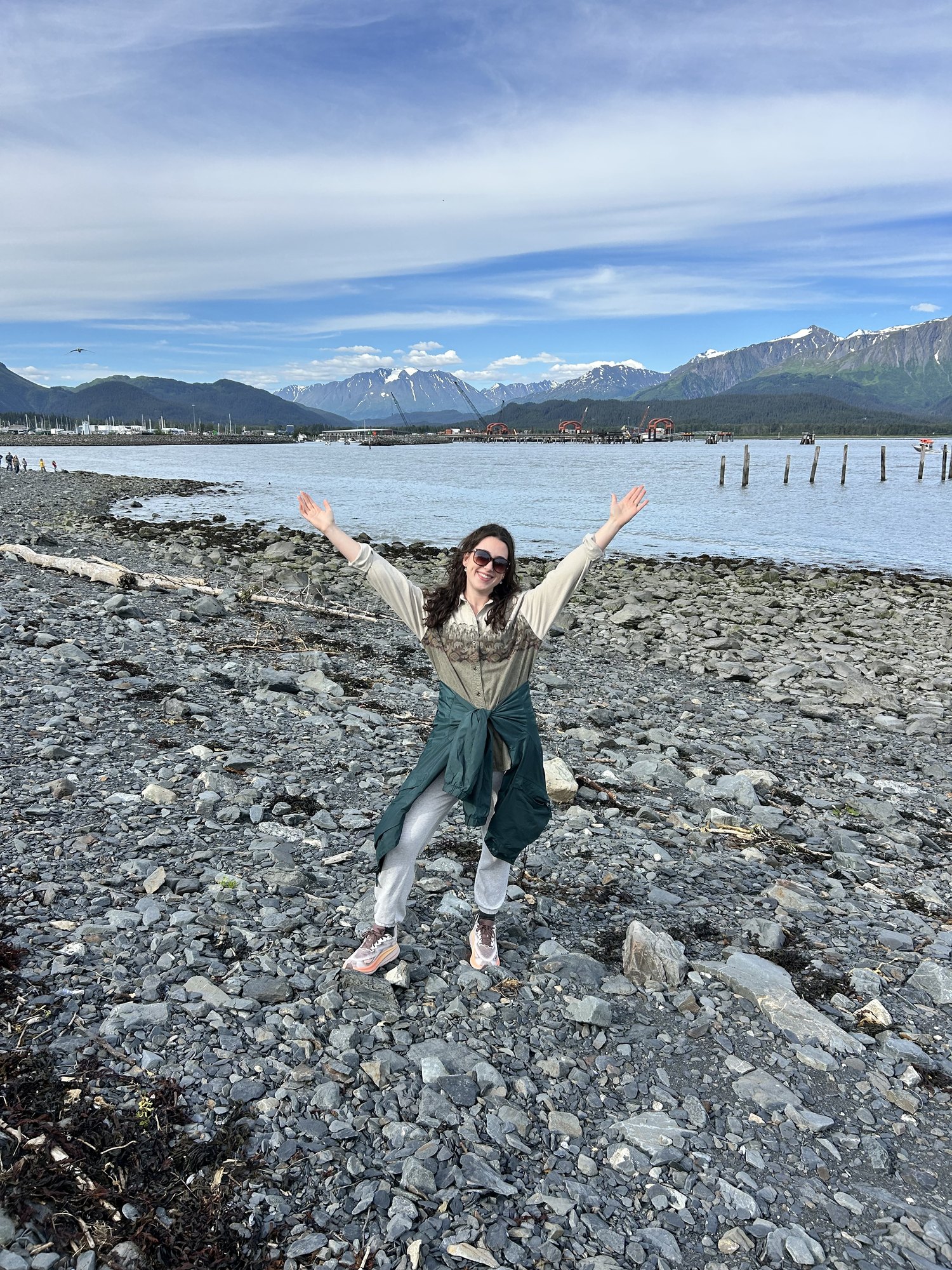 Jess standing on a rocky beach with snow-capped mountains behind her