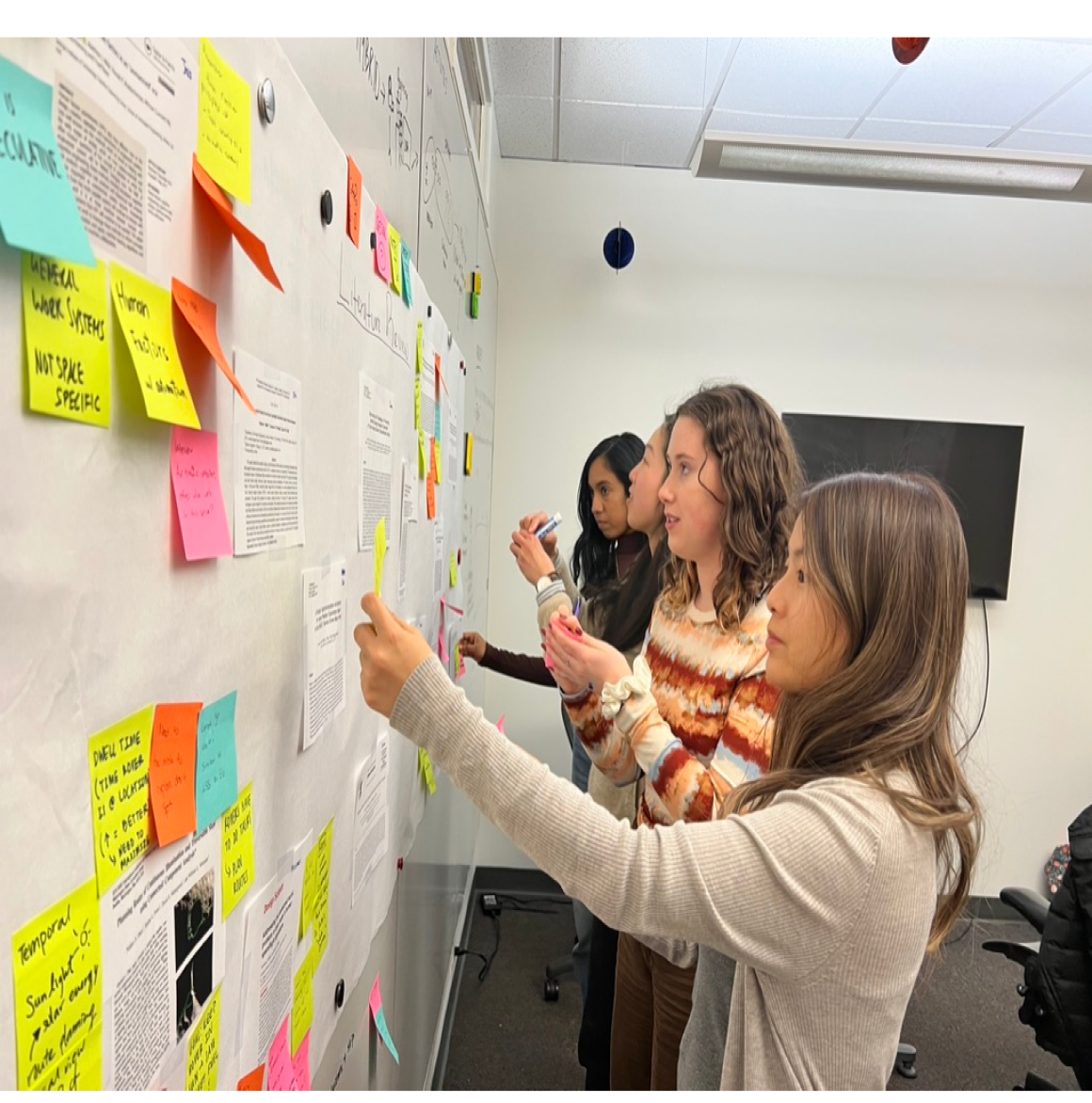 Designers placing sticky notes on a whiteboard to categorize research findings.